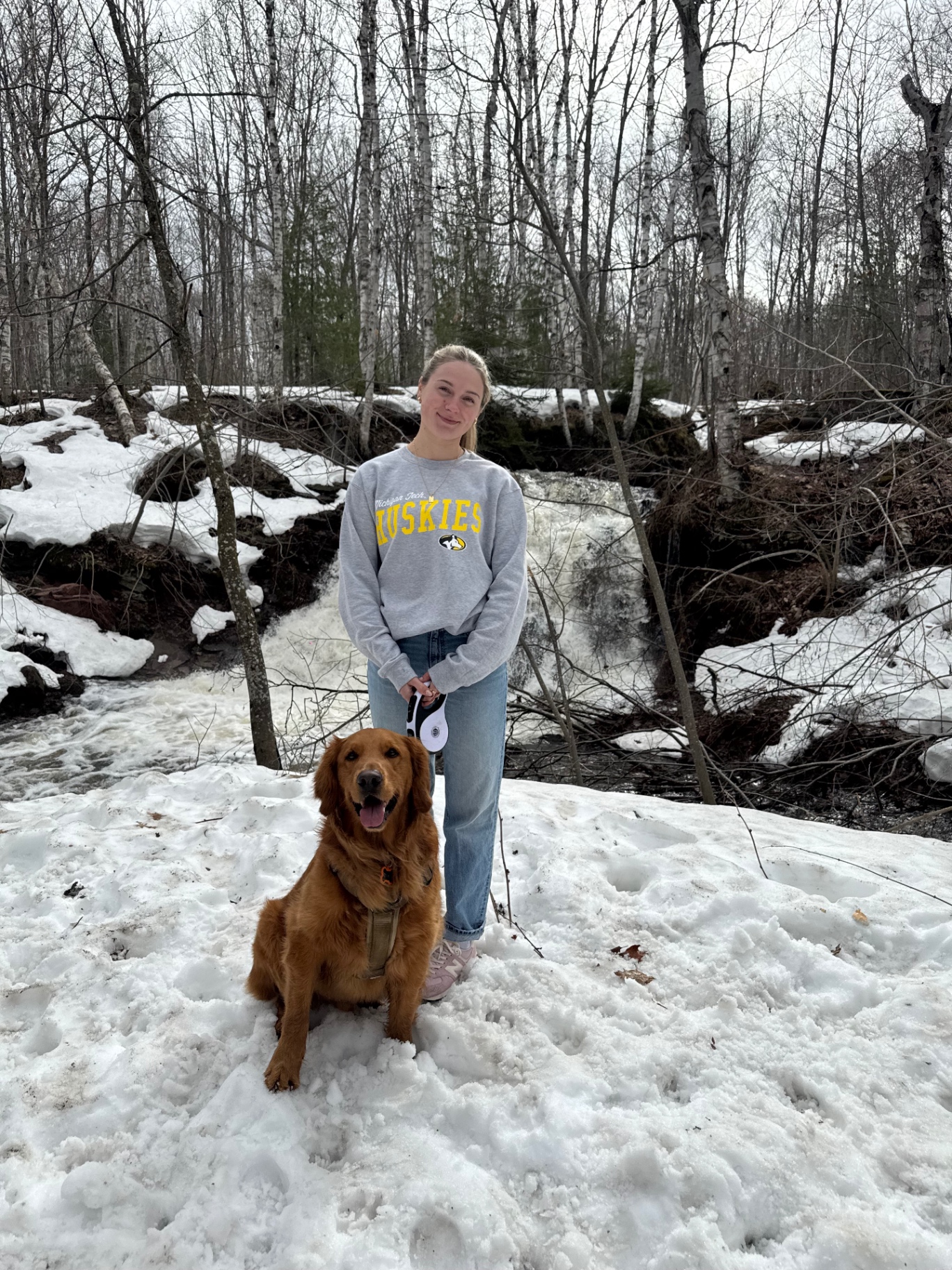 Allie, certified dog groomer, with her golden retriever in a snowy forest